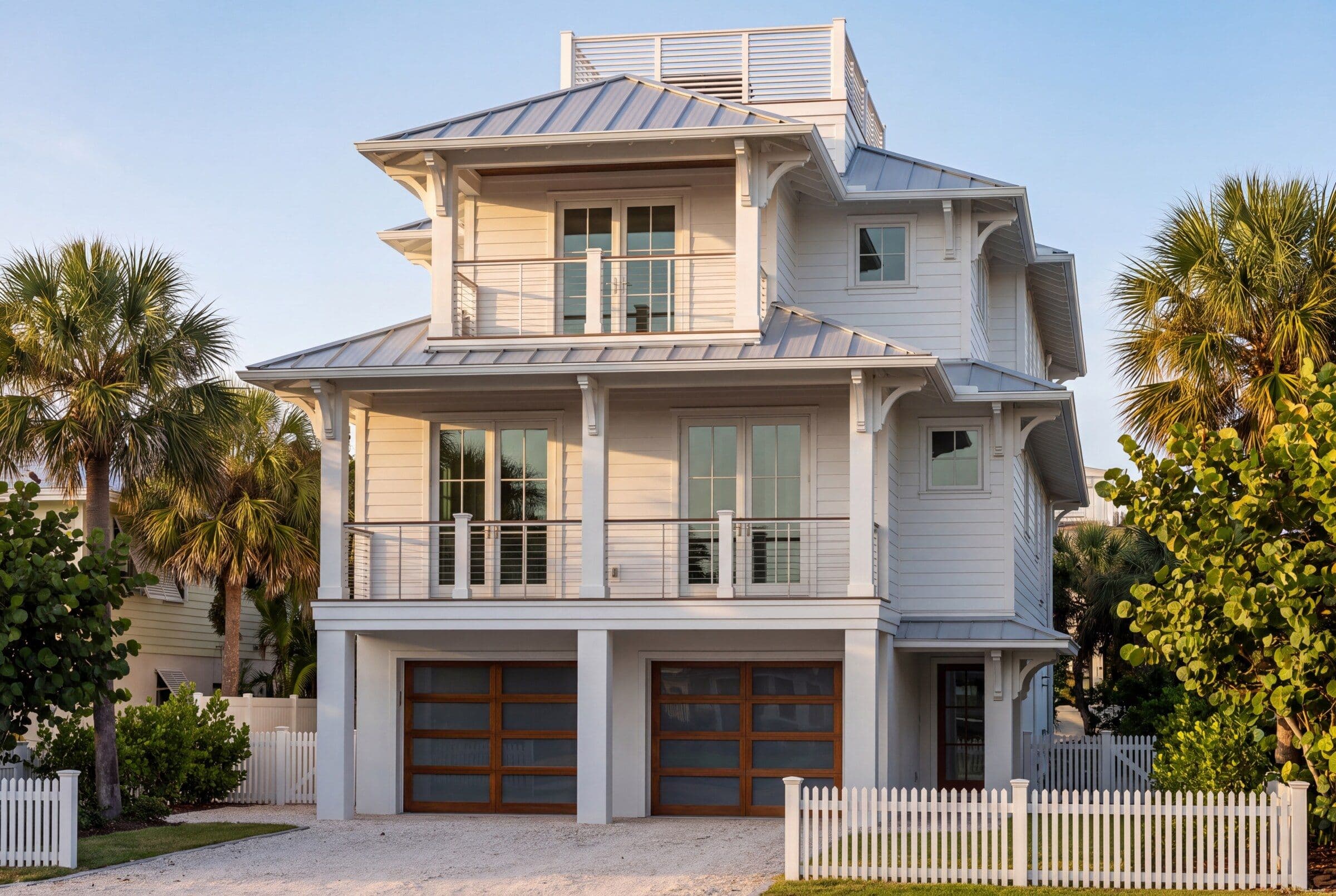 Artist rendering of a three-storey elevated coastal home in white lap siding with metal hip roofs, palms and a shell drive