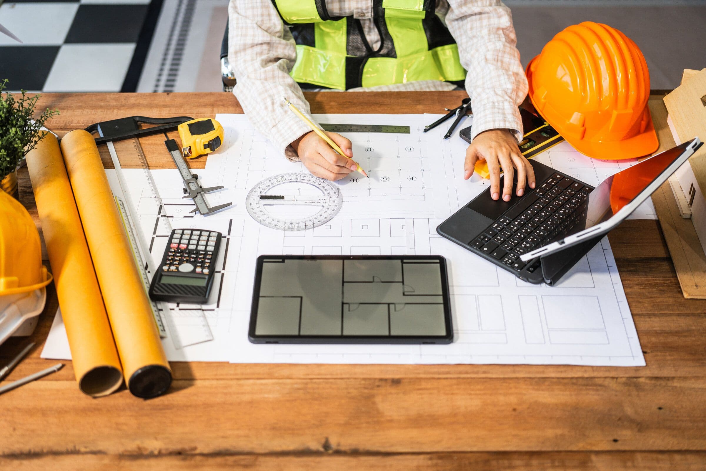 An architect's desk: rolled drawings, a hard hat, a scale rule and a set of plans under review