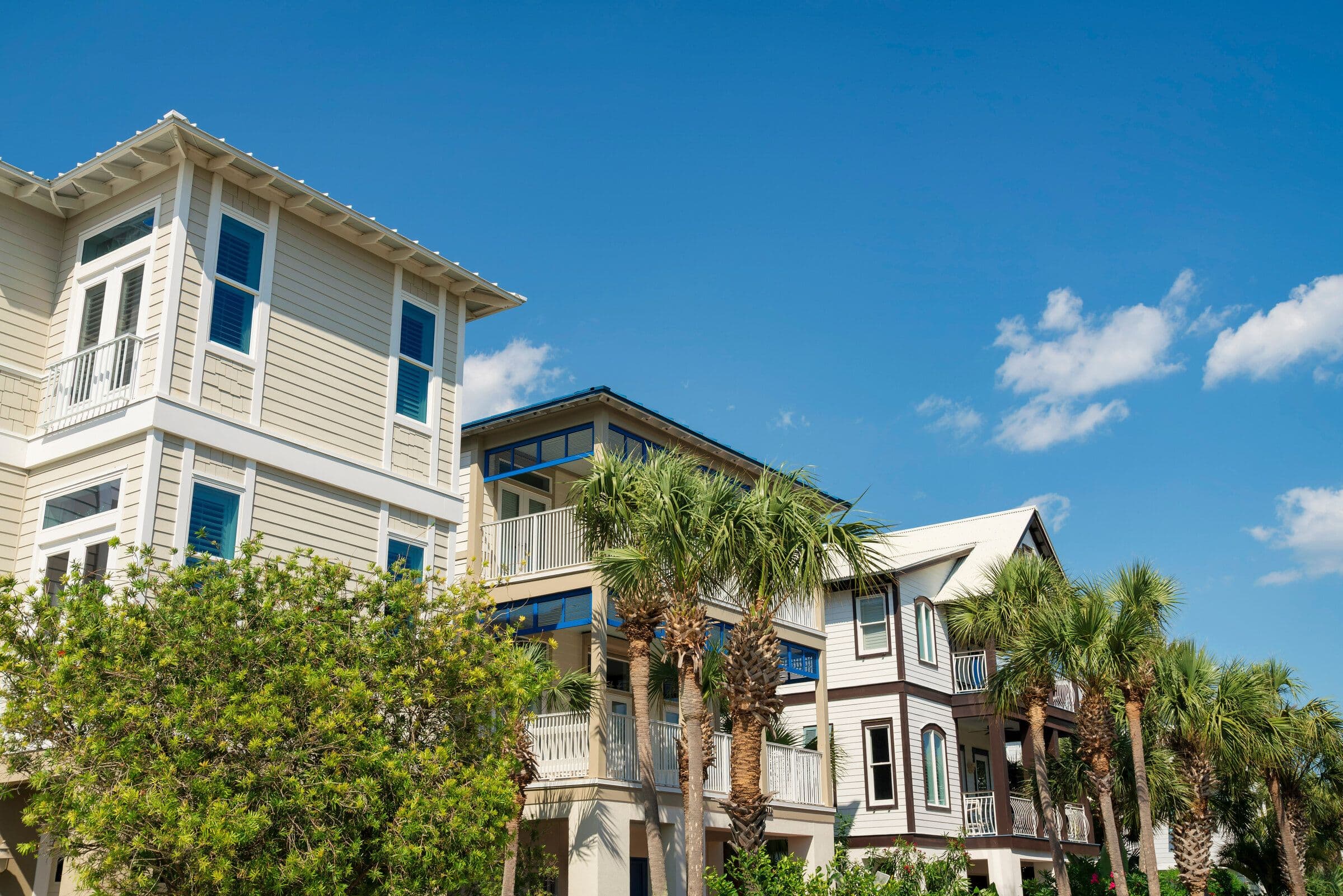 A row of elevated coastal Florida homes in pastel lap siding with metal roofs and palms