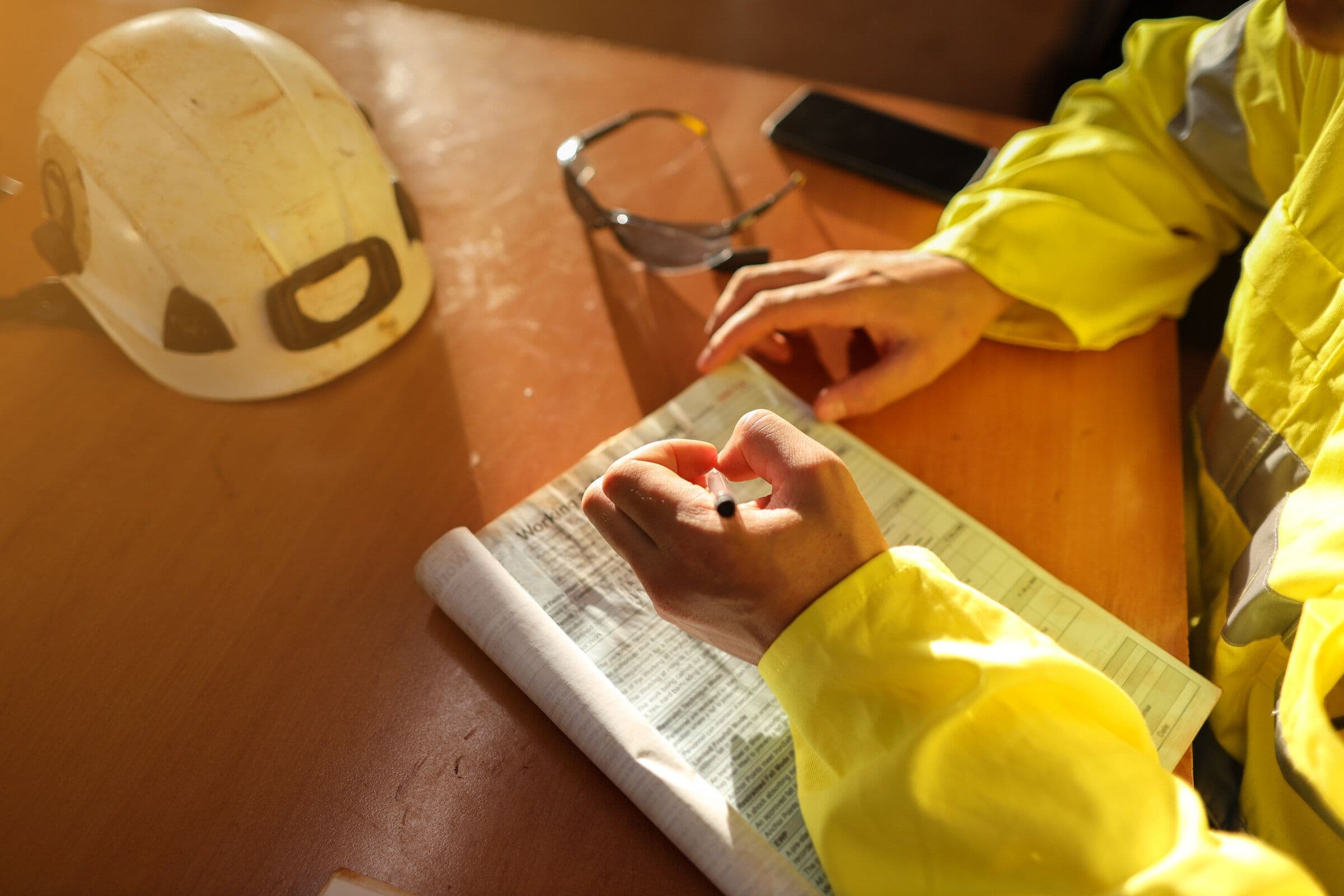 A worker in a hard hat and high-visibility jacket checking a set of construction drawings